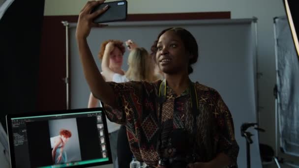 アフリカ系アメリカ人女性フォトグラファーがフォトスタジオで撮影日 バックグラウンドでモデルを準備するスタイリスト — ストック動画