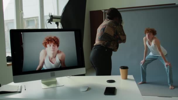 Fotógrafo Fêmea Tirando Fotos Jovem Modelo Masculino Contra Parede Cinza — Vídeo de Stock