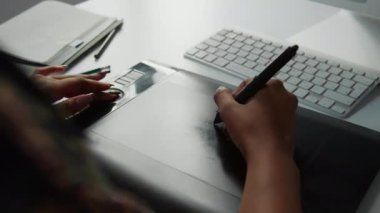 Masadaki grafik tabletine stilus kalem çizen tanınmayan bir kadının ellerini yakın plan çek.