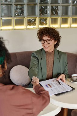 Gülümseyen iş kadını kafeteryada tanımadığı bir kadının elini sıkıyor.
