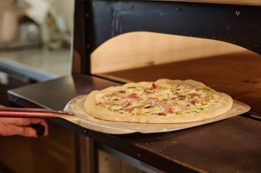 Demir pizza kabuğunun üzerindeki hazır pizzanın yakın çekimi fırından çıkarılıyor.