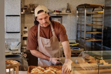 Fırın işçisi kruvasanları demir tepsiden hasır sepetine satıyor.