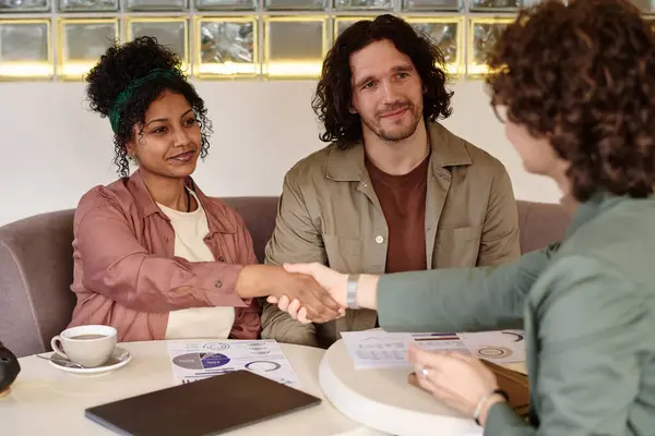 Black girl shaking hand of unknown caucasian woman with young caucasian man sitting next to her
