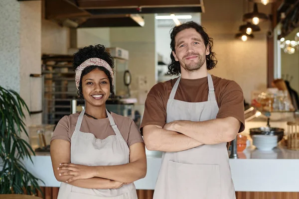 Smiling caucasian man and joyful black woman standing together at their workplace at cafeteria