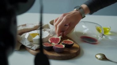 Stüdyo çekimine hazırlanırken taze incir, peynir, bal ve şarap hazırlayan kadın yemek tasarımcısının yakın plan fotoğrafı.