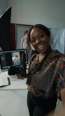 Dik çekimde, elinde dijital fotoğraf makinesi olan genç siyahi kadın fotoğrafçı stüdyoda moda fotoğraf çekimi hazırlığı, video görüşmesi ya da canlı yayın hakkında konuşuyor.