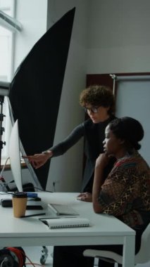 Kadın stilist ve fotoğrafçının bilgisayar ekranındaki fotoğrafa bakıp stüdyoda çekim yapmaya hazırlanırken tartıştıkları dikey bir fotoğraf.