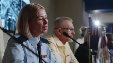 Kadın ordu generali basın toplantısı masasında oturmuş uluslararası zirve sırasında mikrofonla konuşuyor.