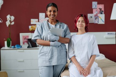 Tabletli başarılı genç estetik cerrah ve yüzünde yükselme izleri olan genç hastası estetik cerrahi kliniklerinin koğuşunda kameraya bakıyor.