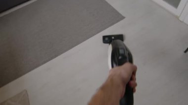 Hafta sonu ev işi yaparken elinde elektrikli süpürgeyle oturma odasında yerleri süpüren tanınmamış bir adamın POV görüntüsü.