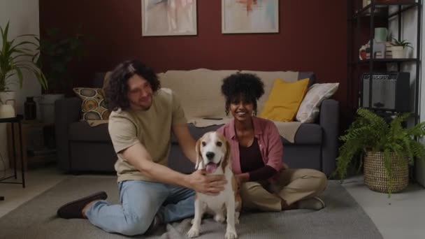 一对年轻的跨种族夫妇和他们的狗在现代客厅的地板上摆姿势拍照的慢幅肖像 — 图库视频影像