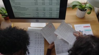 Masaüstü bilgisayar başında birlikte oturarak ev bütçesini yönetirken ve planlarken mali belgelere, faturalara ve makbuzlara bakan genç çiftin üst görünümü