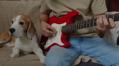 Uzun kıvırcık saçlı, elektro gitar çalan, stüdyo dairesindeki kanepede oturan sevimli av köpeği dinleyen beyaz bir adamın dükkânı.