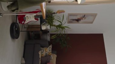 Oturma odasındaki robotik elektrik süpürgesinin dikey görüntüsü. Genç, ırklar arası bir çifte koltukta otururken ve evde keyif çatarken yardım ediyor.