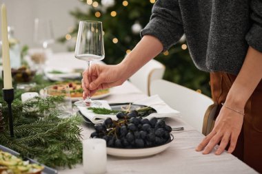 Kimliği belirsiz beyaz bir kadının Noel masasına boş şarap kadehleri koyması.