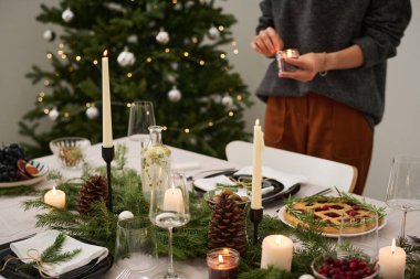 Bilinmeyen bir kadının arka planda mum yaktığı yemek ve süslemelerle dolu bir Noel masası.