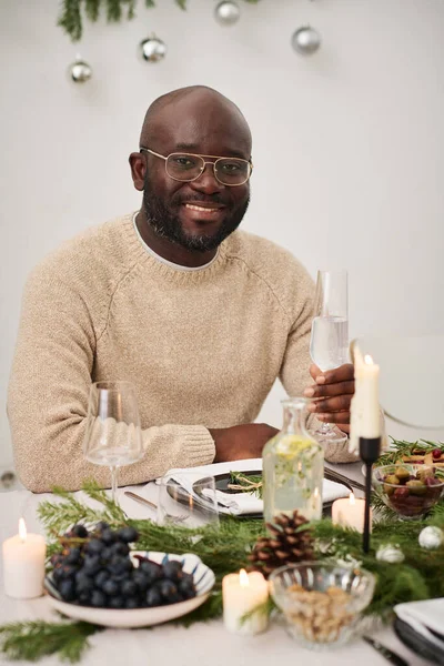 African american christmas party enjoyer sitting at table holding glass with drink smiling at camera