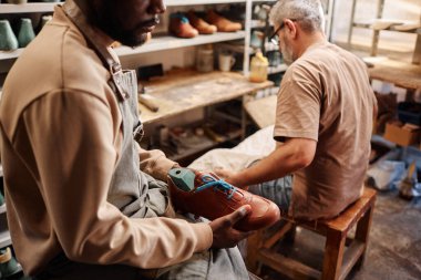 Ayakkabıcının çırak çırağının, elinde çizmeleriyle kameranın önünde efendisine karşı otururken çekilmiş görüntüsü.