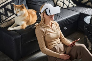 VR kulaklık takan genç bir kadın içeride köpeğiyle birlikte kanepede uyuyor.