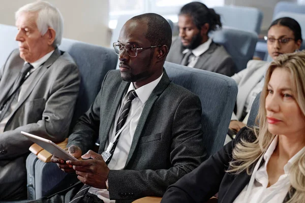 African American businessman in suit using tablet pc while sitting at conference