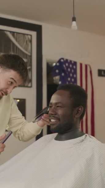 在理发店里 与理发师聊天 用剪发剪修剪头发的黑衣人面带笑容的垂直镜头 — 图库视频影像