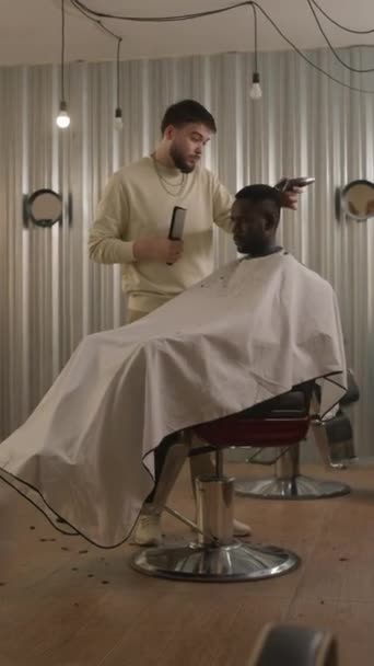美容室のクリッパーと男性クライアントのコンボとトリミング髪のプロのバーバーの垂直フルショット — ストック動画