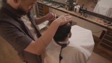 Profesyonel berberin, müşterisinin saçlarını tararken kuaförde saçını keserken yüksek açılı görüntüsü.