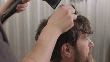 Kuaförde saç kesimi yaptıktan sonra saç kurutma makinesiyle erkek berberin ellerini yakın plan çek.