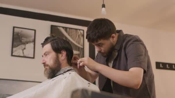 床屋のサロンで男性のひげ付きクライアントにヘアカットしながら 櫛やハサミを使用したバーバー — ストック動画