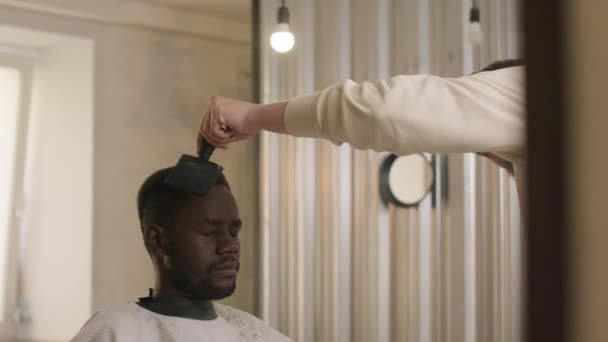 Giovane Uomo Nero Parrucchiere Seduto Nel Salone Mentre Barbiere Spazzolarsi — Video Stock