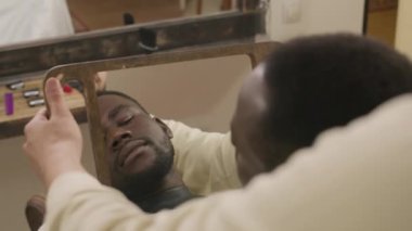 Yeni saç kesimi ve bakımlı sakallı, aynada berbere bakan, iyi bir iş çıkardığı ve gülümsediği için ona teşekkür eden mutlu Afro-Amerikan bir adamın omzundan.