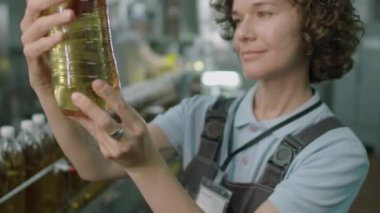 Kadın teknisyen, içki fabrikasında çalışırken şişenin kalitesini limonatayla ölçüyor.