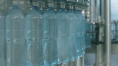 İçecek fabrikasındaki otomatik taşıma hattında saf suyla doldurulan PET şişelerinin orta derecede kapatılması.