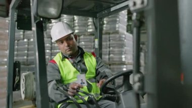 Koruyucu miğferli ve floresan yelekli erkek içki deposu çalışanının paletleri şişelerle doldurduğu görüntüyü büyüt.