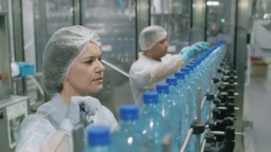 Beyaz önlüklü teknisyenler, içecek fabrikasında damıtılmış suyla PET şişelerini sayıyor.