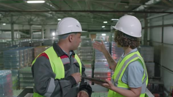 倉庫のデジタルタブレットを使用した配達文書を背景にパレットで議論する2人の労働者の中型ショット — ストック動画