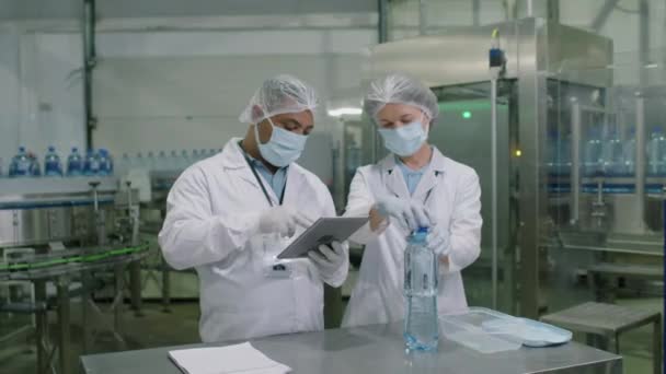 两名配戴拖把帽 手套和白色外套的酒厂化学家从塑料瓶中提取水样的中长镜头 — 图库视频影像