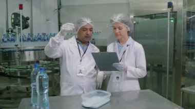 İçki fabrikasında çalışırken iki teknisyenin belgeyi su testiyle doldurduğu orta boy fotoğraf.