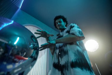 Parlak sanat objesinin yanında ellerini hareket ettiren şık bir adamın düşük açılı görüntüsü.