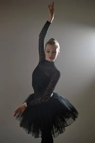Ballerina in black lace leotard and tutu standing in static ballet pose during photoshoot in studio