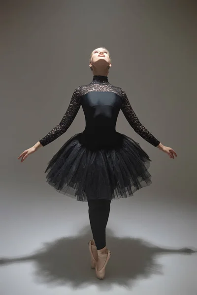 Ballerina in black tutu posing on tiptoes stretching and looking up