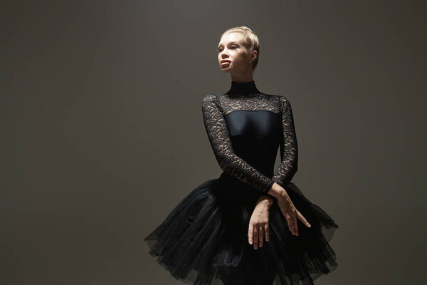 Caucasian ballerina in black lace leotard standing in elegant pose against dark background
