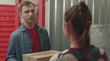 Adam karısıyla konuşuyor ve karton kutuları self servis deposuna taşıyor.