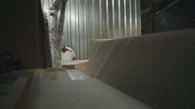 Kişisel eşyalarını kişisel depolama deposunda muhafaza etmek için karton kutuları istifleyen genç bir kadının depolama ünitesinden görüntüsü