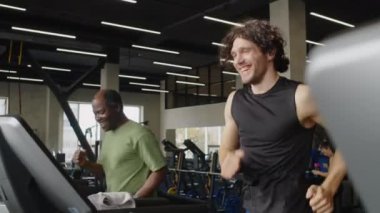 Orta boy erkek eğitmen ve motivasyonlu orta yaşlı adamın spor salonunda spor yaparken koşu bandında koşması.