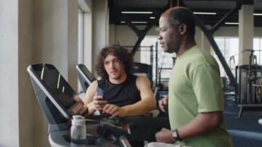 Spor salonundaki koşu bandında orta yaşlı Afrikalı Amerikalı bir adama yardım ederken elde çekilen fotoğraf.