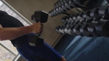 Spor salonundaki dambılları kullanarak kaslarını geliştiren genç sporcunun görüntüsü.