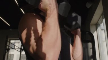 Sporcunun düşük açılı kıvrımları, kollarında ve omuzlarında dambıllar, beden eğitimi sırasında kas yapıyor.