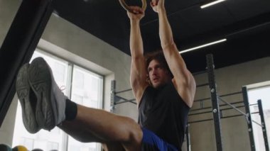 Spor salonunda kol kaslarını çalıştırırken düşük açılı güçlü beyaz adam jimnastik halkaları kullanıyor.