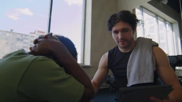 在健身房锻炼的过程中 用数码平板电脑拍下了快乐的男性教练 并激励中年男人做仰卧起坐的动作 — 图库视频影像